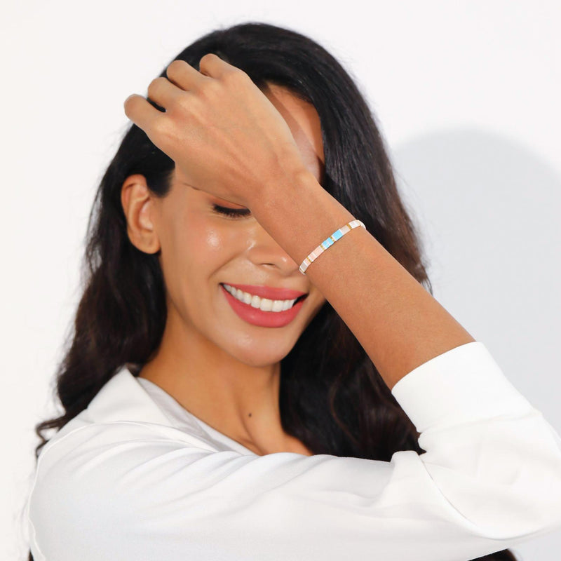 Woman with dark hair and a white shirt smiling with one hand on her head.