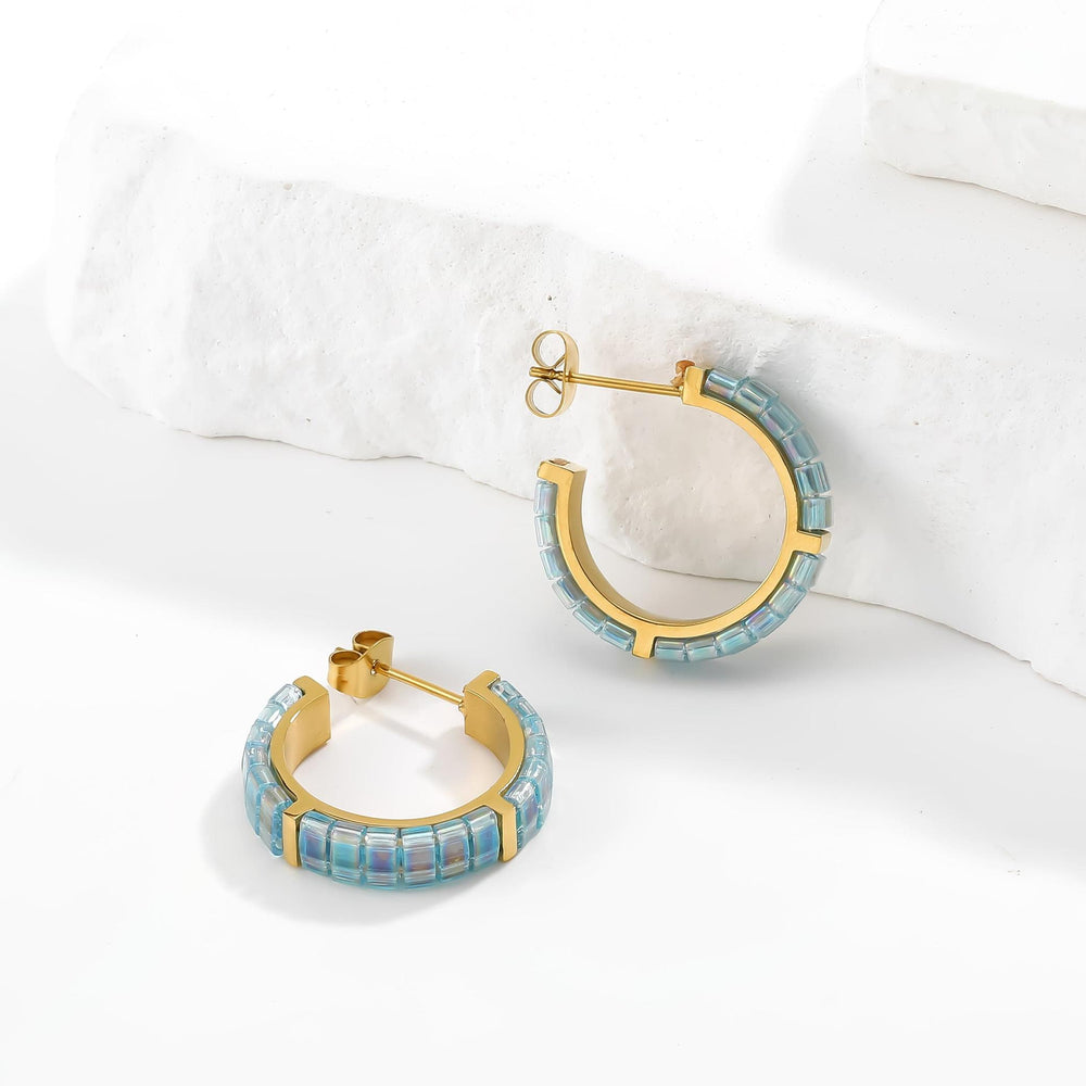Gold hoop earrings with blue gemstones on a white surface
