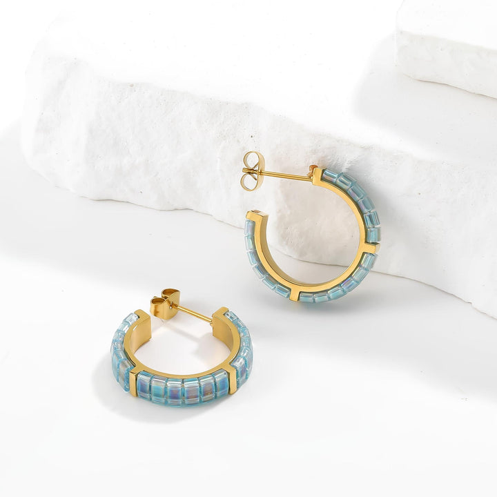 Gold hoop earrings with blue gemstones on a white surface